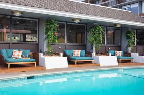 Resort poolside lounge area with turquoise seating, tropical plants, and large windows