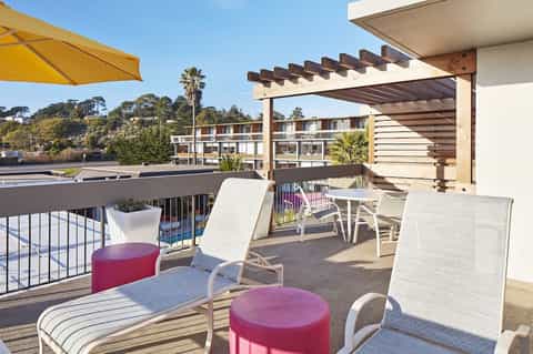 Modern resort balcony with lounge chairs, pergola shade structure, and poolside amenities overlooking water