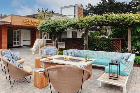 Outdoor patio with fire pit, turquoise sectional seating, woven chairs, and grapevine pergola at Carmel Mission Inn