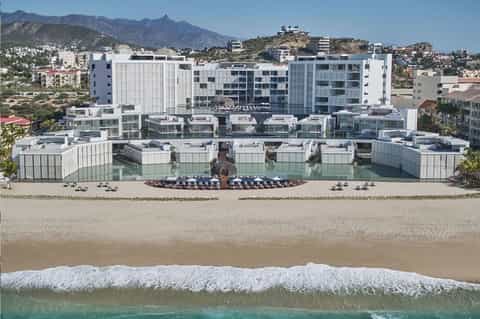 Beachfront resort with white modern architecture, loungers, and mountains in background