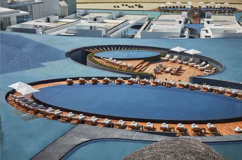 Aerial view of luxury resort with multiple circular pools, wooden decking, and lounge areas