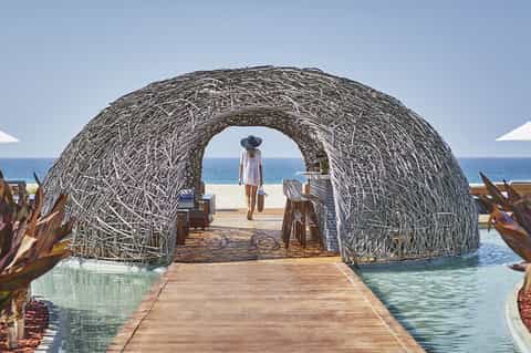 Woven archway walkway leading to beach with ocean view and tropical landscaping