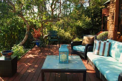 Wooden deck patio with wicker seating, striped cushions, and natural tree canopy overhead