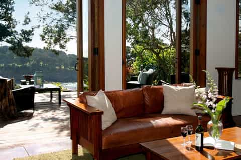 Luxury lakeside living room with brown leather sofa, large windows, and forest views