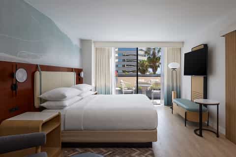 Contemporary hotel room with king bed, flat-screen TV, balcony access, and modern wood accents