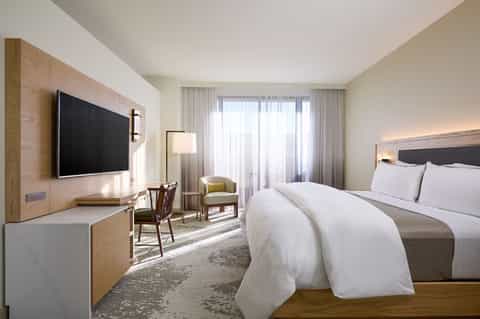 Contemporary hotel room with flat-screen TV, wooden accent wall, and seating area with ocean views