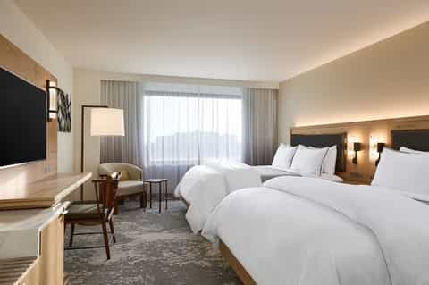 Modern hotel bedroom with two double beds, desk, and balcony with ocean views