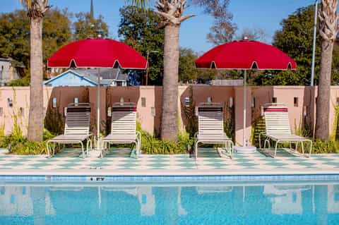 Poolside lounge area with red umbrellas, white loungers, and tan building backdrop