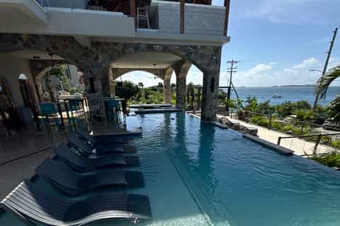 Infinity pool under stone arches with ocean views and lounge chairs on wooden deck