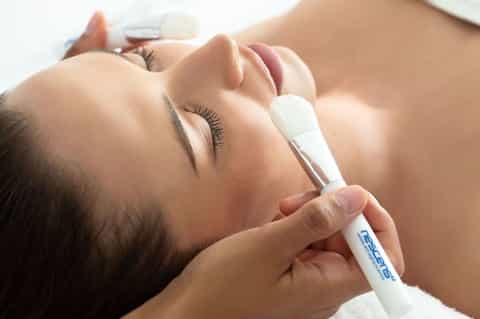Woman receiving facial treatment with handheld device at spa