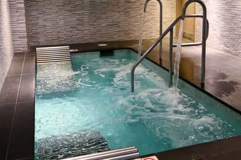 Indoor hot tub with thermal water jets and black metal railings in spa facility