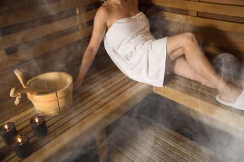 Woman in white towel relaxing in hot spring bath with candles and wooden bucket