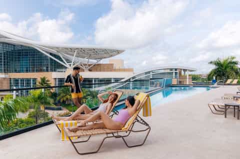 Rooftop pool area with yellow-striped lounge chairs, modern curved architecture, and city skyline views
