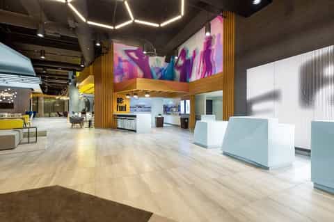 Contemporary hotel lobby with colorful abstract mural, geometric ceiling lights, wooden accents, and white reception desk