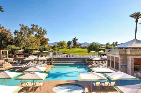 Resort pool complex with lounge chairs, umbrellas, hot tub, and golf course views