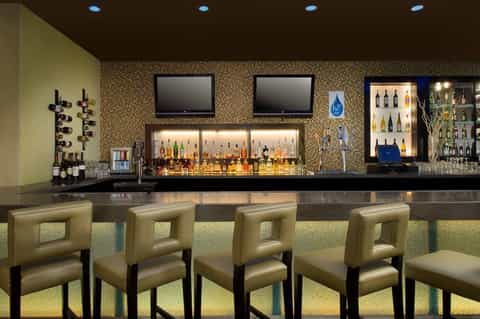 Upscale bar with illuminated bottles, mosaic tile backsplash, and cream-colored bar seating