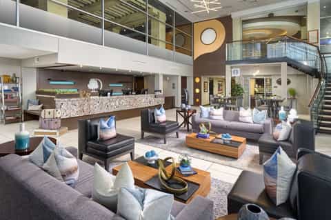Modern hotel lobby with two-story atrium, multiple seating areas, decorative pillows, and marble reception desk