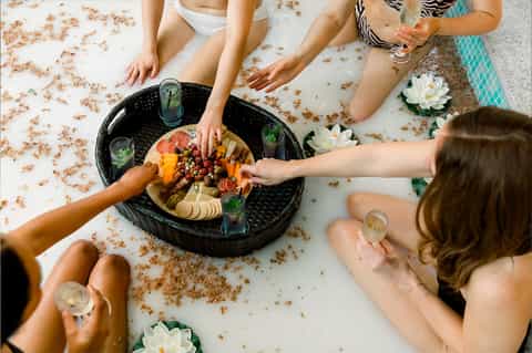 Overhead view of friends sharing a charcuterie platter on a white surface with water lily decorations