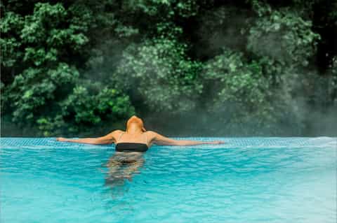 Man in infinity pool overlooking lush forest canopy in tropical resort setting