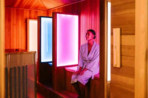 Woman in robe inside illuminated sauna with neon pink and blue lighting
