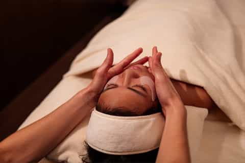 Spa therapist giving a relaxing facial massage to a client lying in bed with a headband