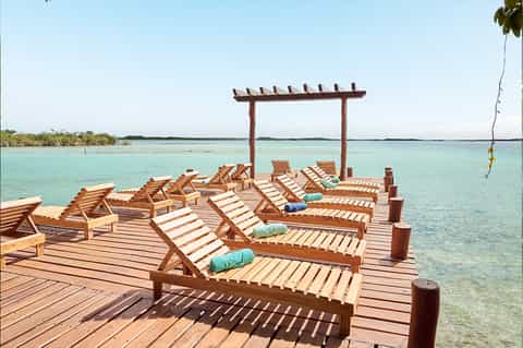 Wooden dock with lounge chairs and pergola overlooking turquoise lagoon waters