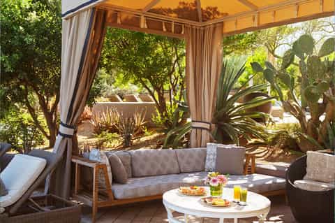 Covered outdoor patio with comfortable seating, tropical plants, and a white round table with refreshments