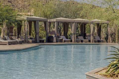 Resort pool with multiple dark cabanas and desert landscape with cacti
