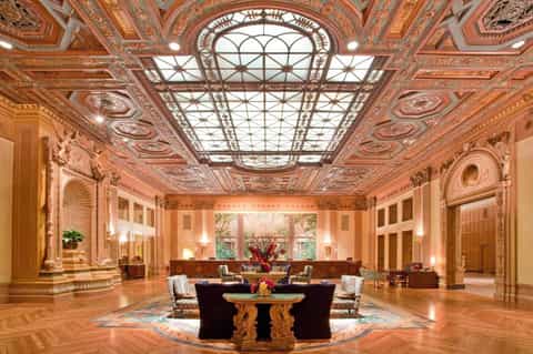 Grand ornate ballroom with decorative ceiling, skylight, marble floors, and central furniture arrangement