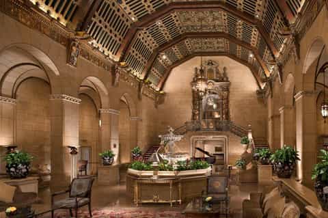 Grand historic hotel lobby with ornate coffered ceiling, arched columns, and decorative plants