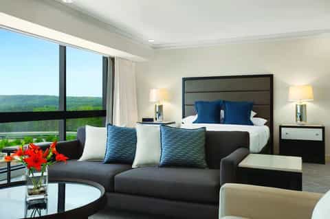 Luxury hotel suite with panoramic window view of green landscape, modern furnishings, and king bed