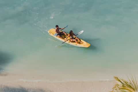 Couple kayaking in turquoise shallow water near sandy beach with palm trees