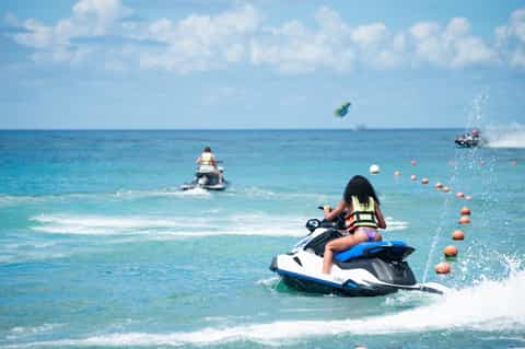 Jet skis racing through turquoise ocean water near sandy beach
