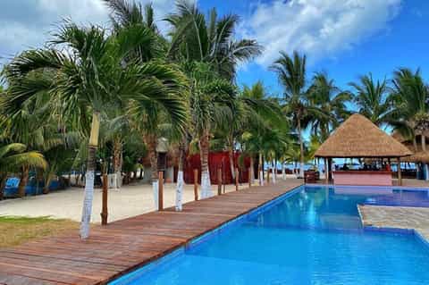 Beachfront resort with two pools, wooden deck, palm trees, thatched-roof bar, and ocean view