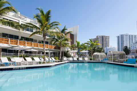 Modern waterfront pool with white loungers, palm trees, and high-rise apartment buildings