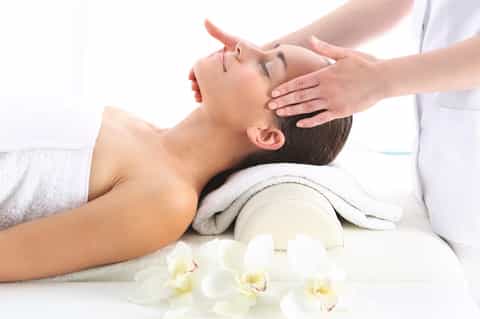 Woman receiving head massage at spa with white orchids and towels in relaxing setting