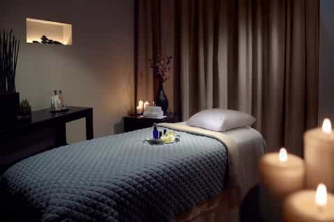 Spa treatment room with massage table, candles, dark wood furnishings, and ambient lighting