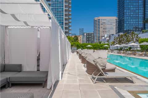 Resort pool deck with white cabanas, lounge chairs, umbrellas, and city skyline backdrop on clear day