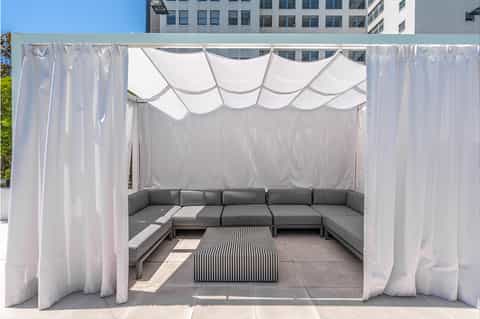 Outdoor cabana with white sheer curtains and gray sectional sofa on rooftop terrace