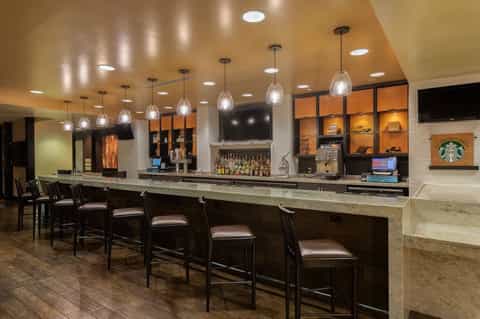 Hotel bar with long counter, pendant lighting, shelved bottles, and Starbucks logo
