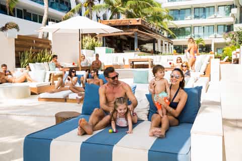 Family relaxing on blue and white striped loungers at beach resort pool area