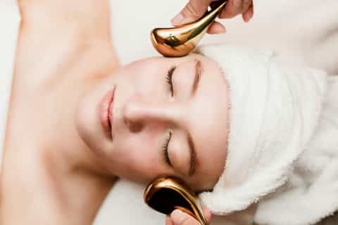 Spa facial treatment with gold gua sha tool applied to client's forehead