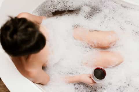 Child's hands playing in bubble bath with soap suds and holding a cup