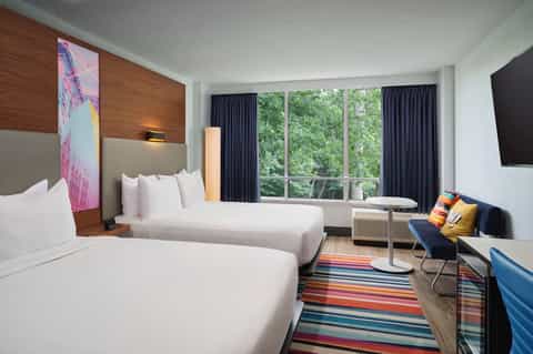 Hotel room with two queen beds, wood headboard, large windows, and colorful striped rug