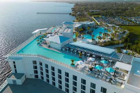 Aerial view of beachfront resort with turquoise pools, water slides, palm trees, and bay views