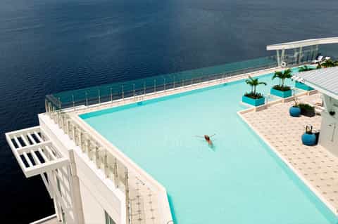 Turquoise infinity pool overlooking ocean with white railings and palm plants