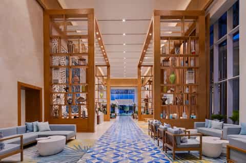 Luxury hotel lobby with wooden shelving, blue patterned flooring, and contemporary seating
