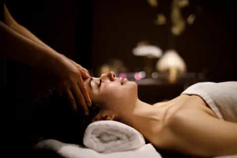 Woman receiving relaxing head massage at spa with white towels and ambient lighting