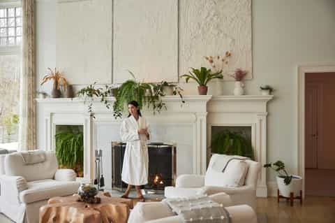 Elegant living room with white fireplace, decorative plants, artwork, and neutral upholstered furniture