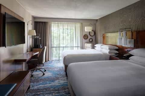Modern hotel room with two queen beds, desk, TV, and sliding glass doors to balcony